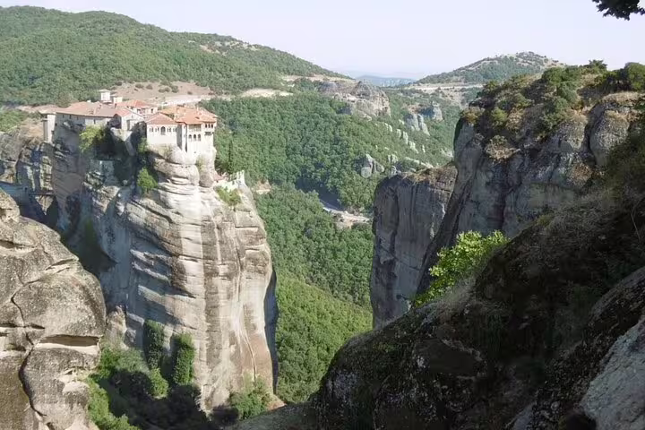 Cliffside Meteora monastery above lush valley, panoramic viewpoint on Meteora private day tour from Athens