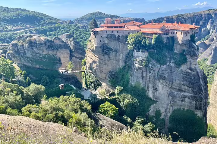 Panoramic view of Meteora cliff-top monastery with red roofs and lush valleys on a full-day private tour