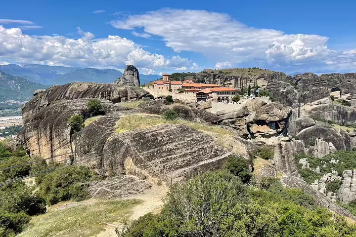 Meteora monastery atop dramatic rock pillars under blue skies, highlight of a full-day private tour in Greece