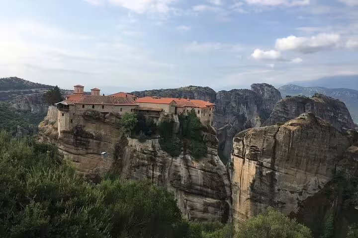 Meteora monastery with red roofs perched on dramatic rock pillar, highlight of private Athens day trip