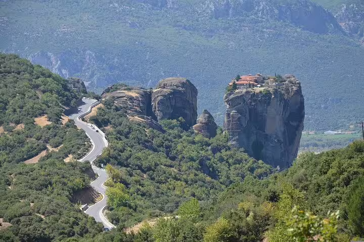 Scenic view of winding road leading to Meteora monastery perched on towering rock, ideal for private tours from Athens.