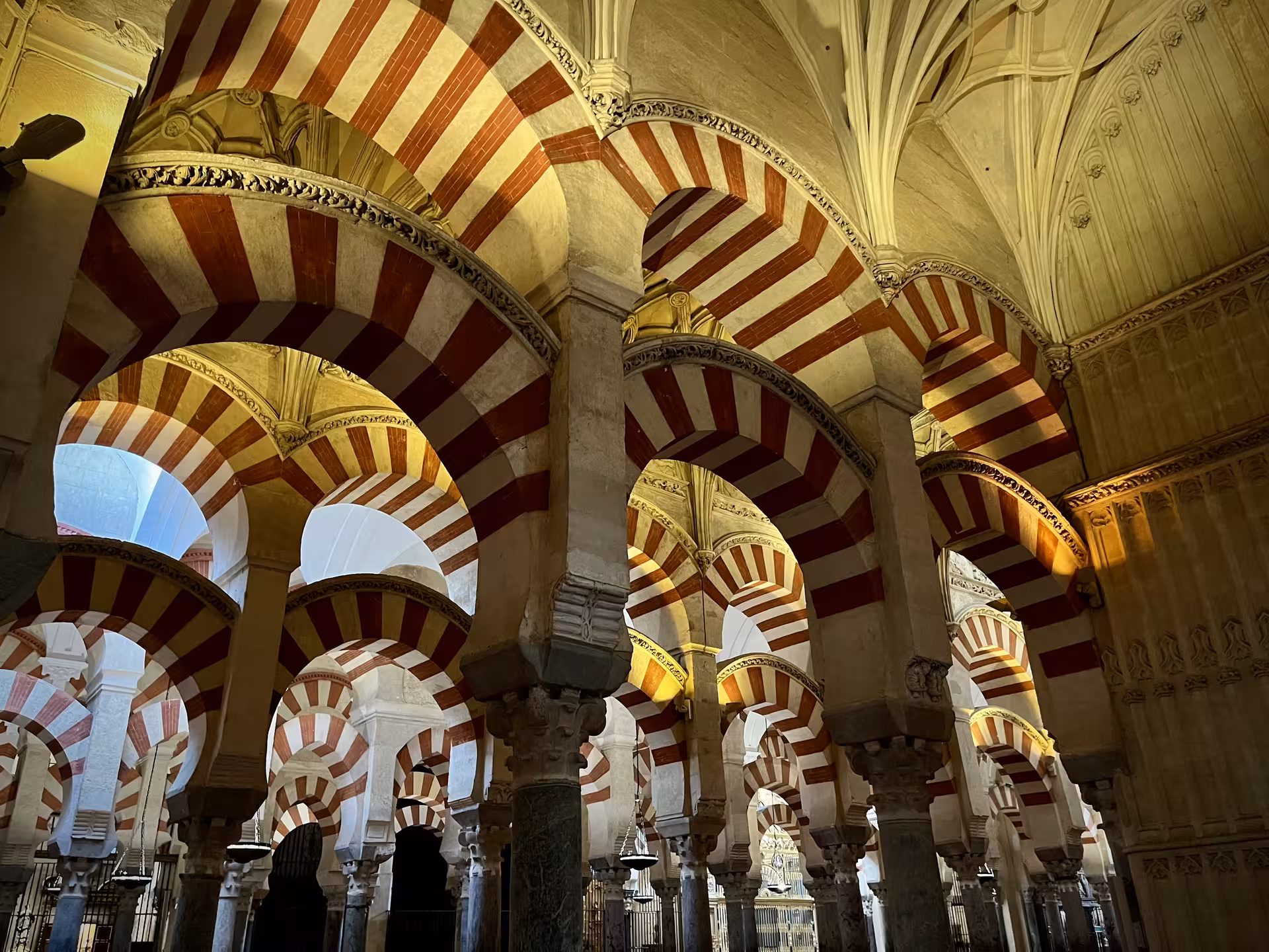 Golden-lit horseshoe arches and stone columns in the Mezquita of Córdoba on Monumentos Locales visit