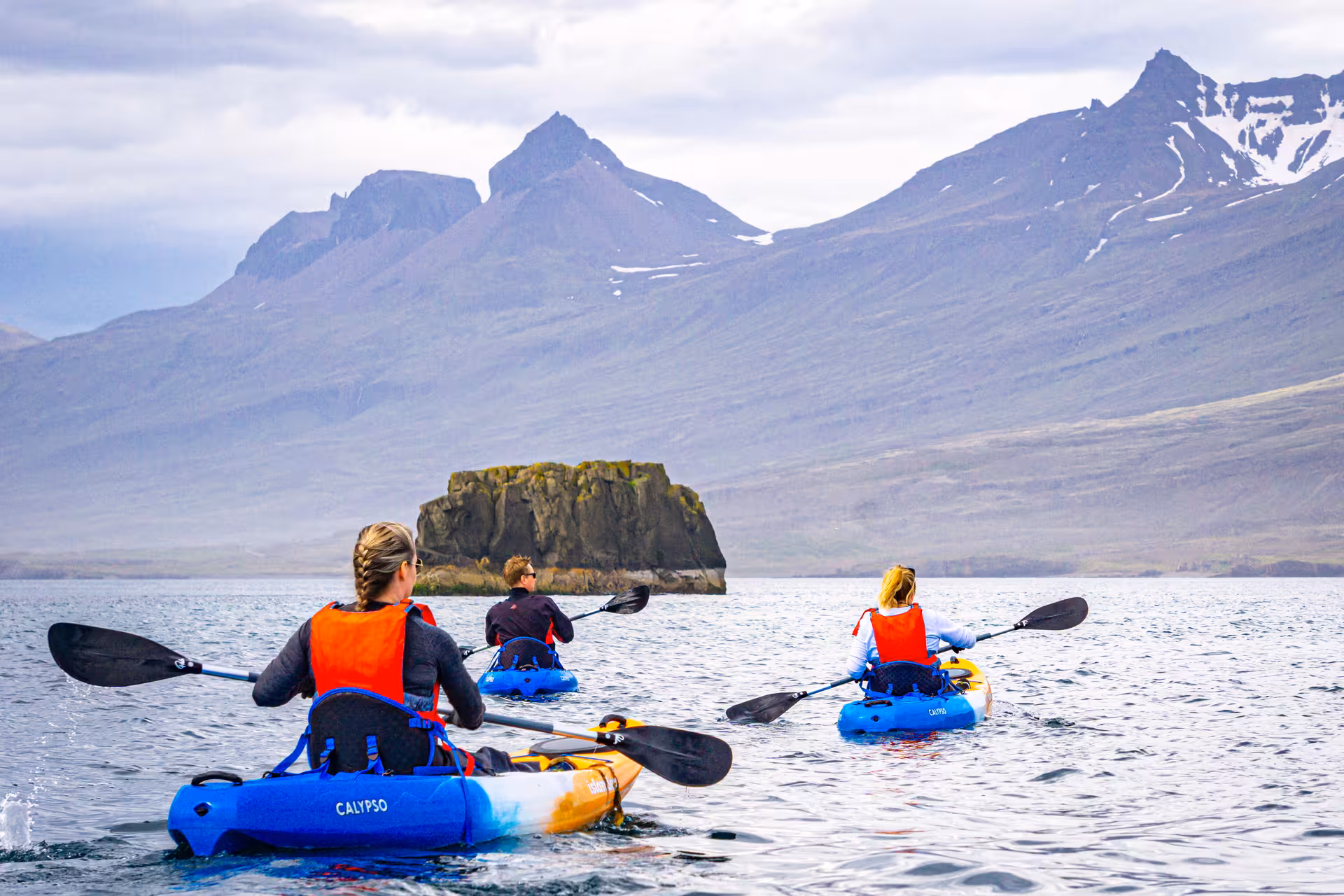 Group of kayakers explore serene waters with majestic mountains in the background on a midnight tour.