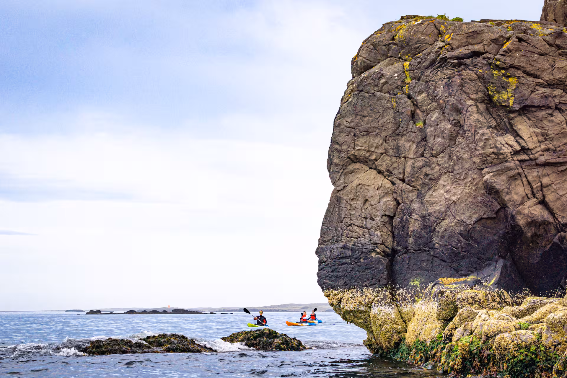 Kayakers navigate around a towering rock formation in the ocean, highlighting the adventure of a midnight tour.