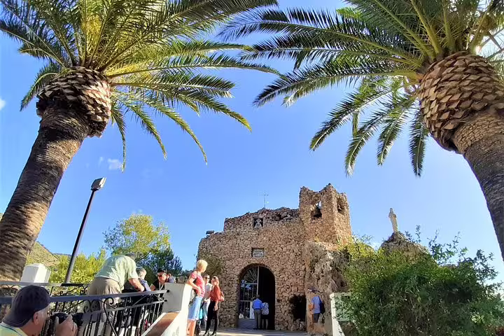 Group visit to Mijas viewpoint by stone chapel framed by palm trees on Costa del Sol day trip