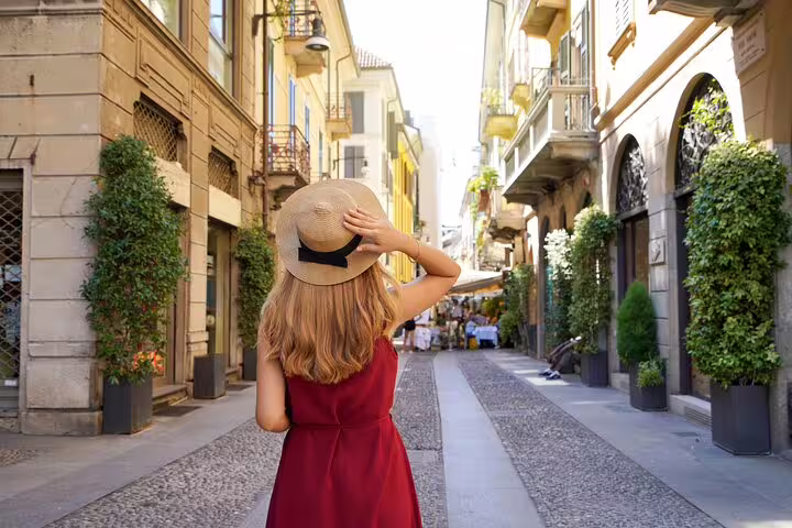 A woman in a red dress explores a charming, sunlit street in Milan during a private 2-hour tour for newcomers.