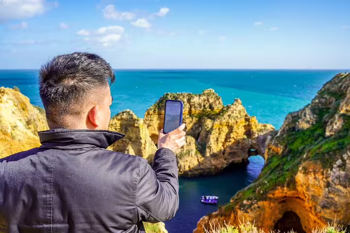 Traveler capturing stunning view of Algarve coastline with Benagil caves during private tour from Milfontes, Portugal.