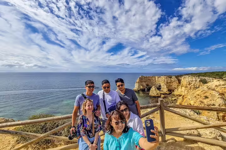 Group enjoying scenic view on Milfontes to Algarve tour with a boat trip to Benagil caves, capturing memories by the cliffs.