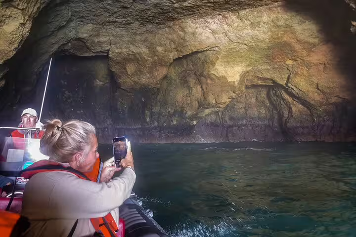 Tourists on a boat explore the stunning Benagil caves during a private tour from Milfontes to the Algarve, capturing photos.