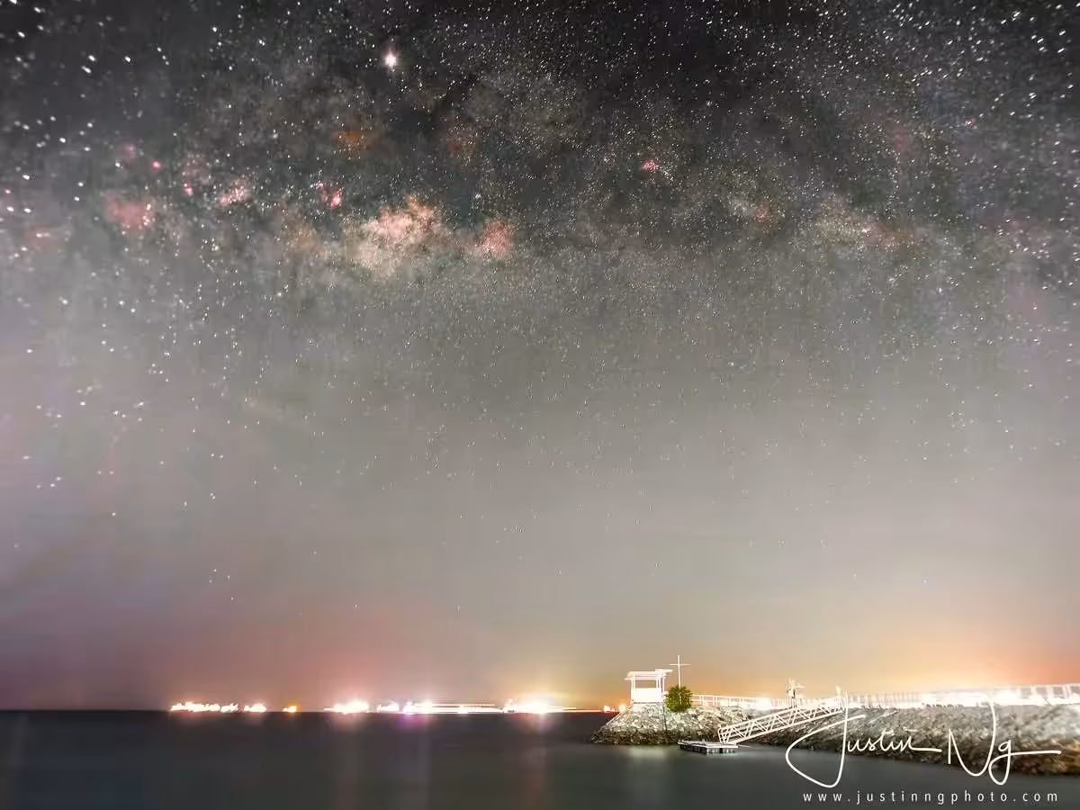 Milky Way sparkles over a serene waterfront in Singapore, featured in Justin Ng's night photography workshop.