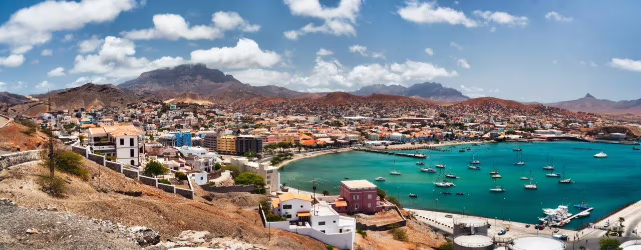 Scenic view of Mindelo Bay in São Vicente, Cape Verde, featuring vibrant coastal cityscape and anchored sailboats under blue skies.