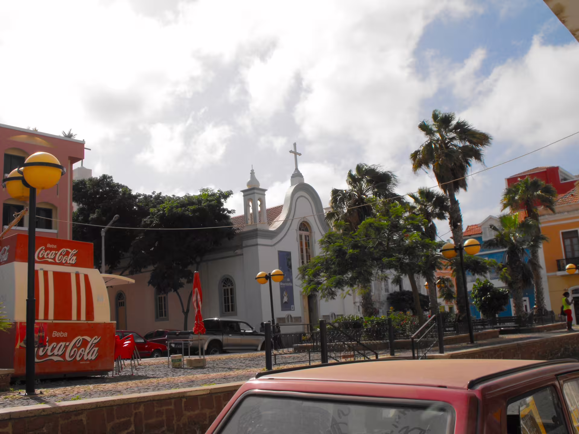 Colorful Mindelo street scene with historic church, palm trees, and vintage architecture, perfect for a vibrant city walking tour.