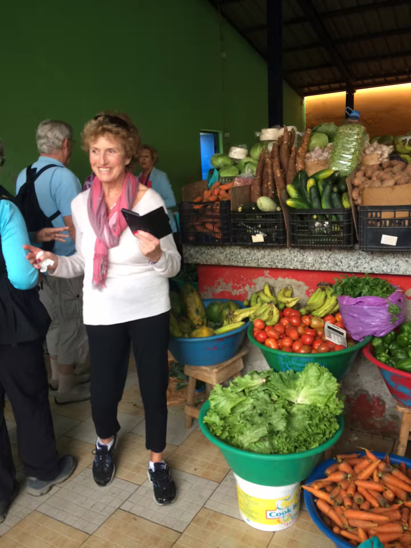 Tourists explore a vibrant local market in Mindelo, São Vicente, featuring fresh produce like lettuce, tomatoes, and carrots.