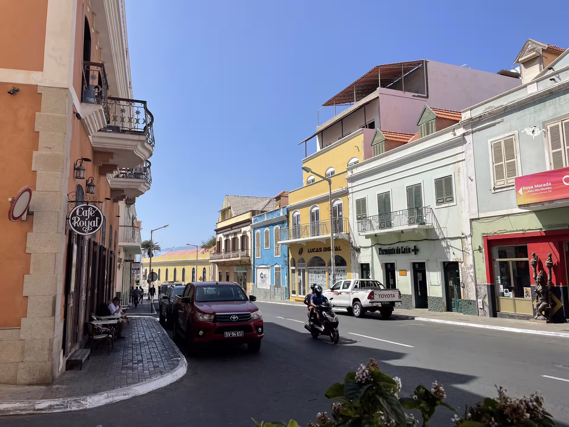 Colorful colonial architecture lines a bustling street in Mindelo, São Vicente, showcasing vibrant local life on a sunny day.