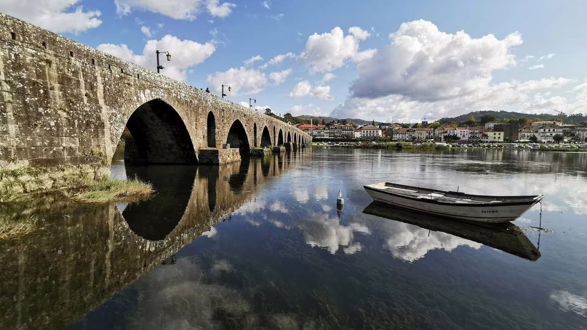 Beautiful arched stone bridge reflected in river with a small boat, highlighting Minho Region's charm.