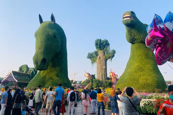 Ras Al Khaimah Adventure Await ticket scene with crowds in floral park beside giant horse and dinosaur topiaries