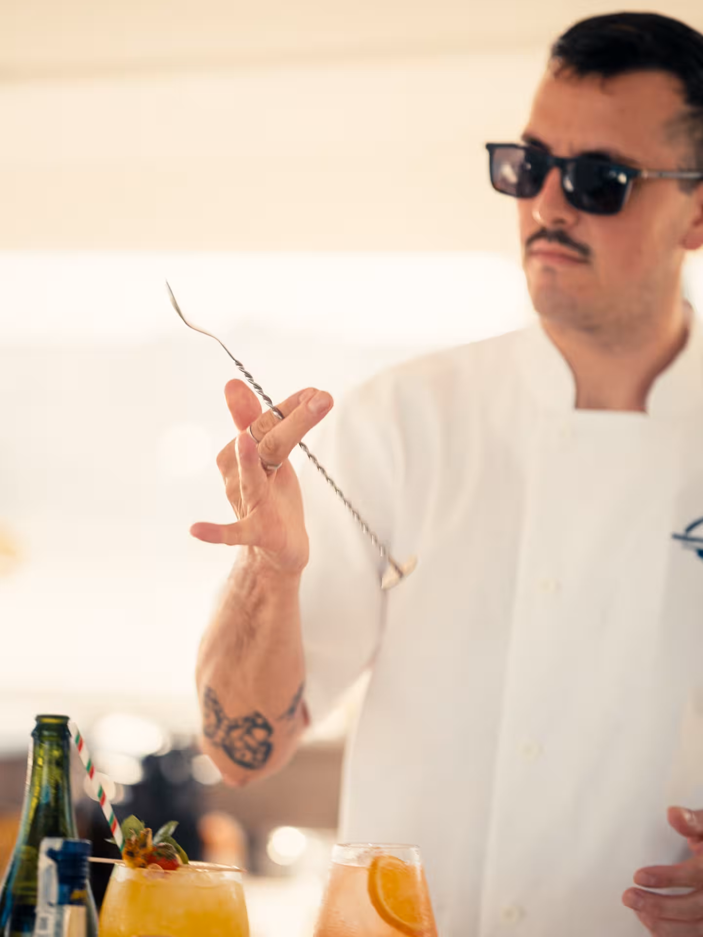Mixologist in sunglasses demonstrates bar spoon technique during hands-on cocktail masterclass with crafted drinks