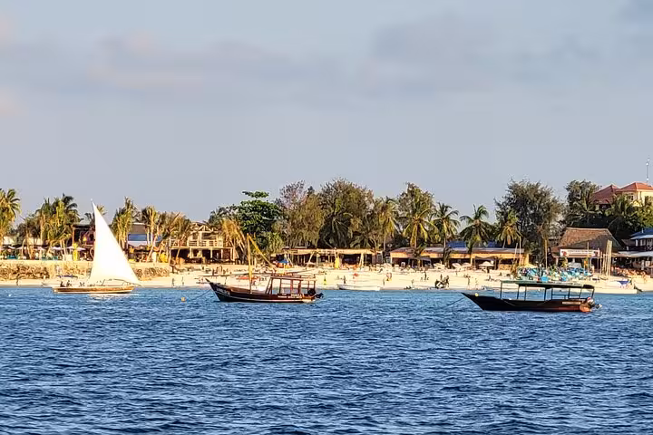 Scenic view of dhows sailing near Mnemba Island's sandy beaches, part of the unforgettable Zanzibar snorkeling tour.