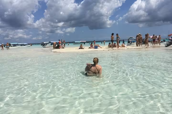 Visitors bask in the shallow, turquoise waters of Mnemba Island, surrounded by boats and vibrant beach activity.