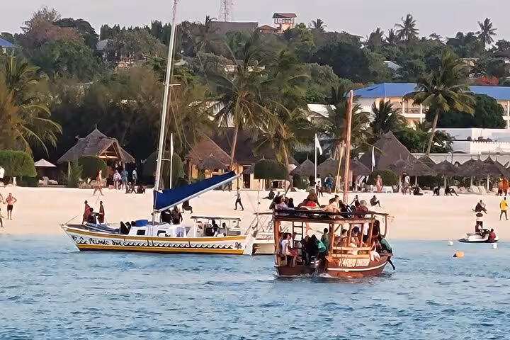 Tourists enjoy a vibrant boat tour near the sandy shores of Zanzibar's Mnemba Island, ideal for dolphin watching and snorkeling.