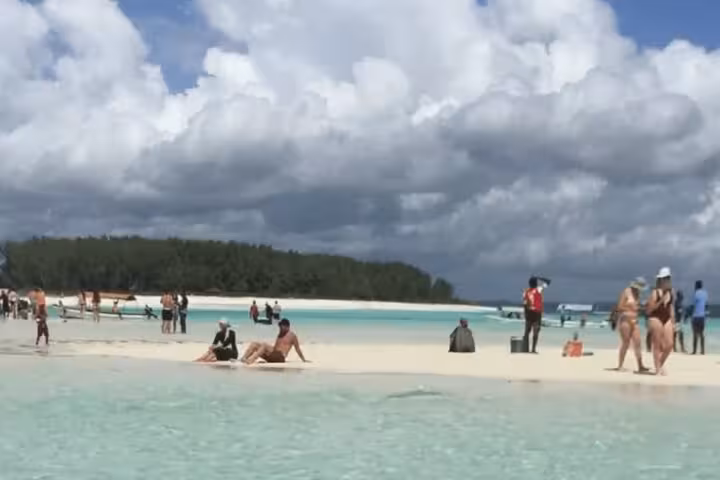 Tourists relax on the pristine sandy shores of Mnemba Island, enjoying the crystal-clear waters and tropical surroundings.