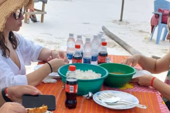 Guests enjoy a beachside meal with refreshing drinks on Mnemba Island, part of an adventurous Zanzibar snorkeling tour.