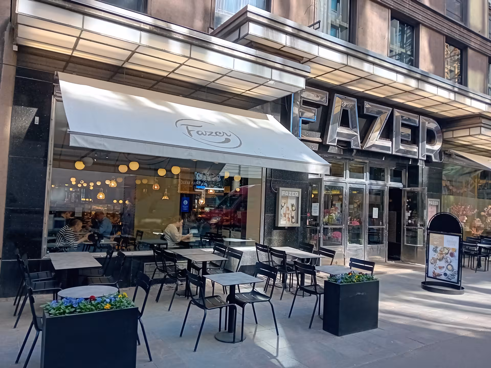 Outdoor view of a modern cafe with a large Fazer sign and inviting patio seating, perfect for an architecture tour stop.