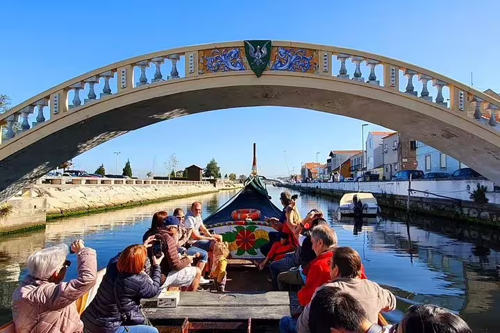 Visitors capture stunning views from a Moliceiro boat under a picturesque bridge on Aveiro's scenic waterways.
