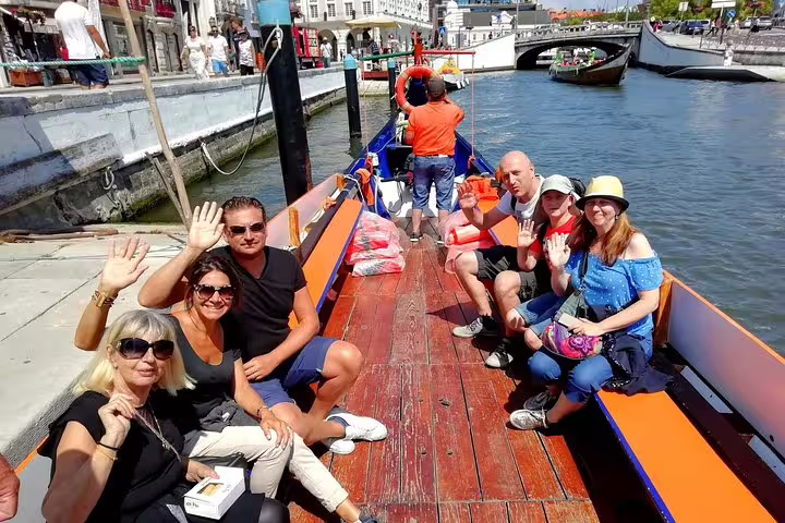 Happy tourists wave during a vibrant Moliceiro river cruise in Aveiro, experiencing Portugal's unique canal culture.