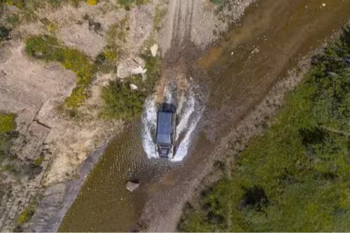 Aerial view of an off-road vehicle crossing a stream surrounded by lush greenery near Monchique, ideal for adventure tours.