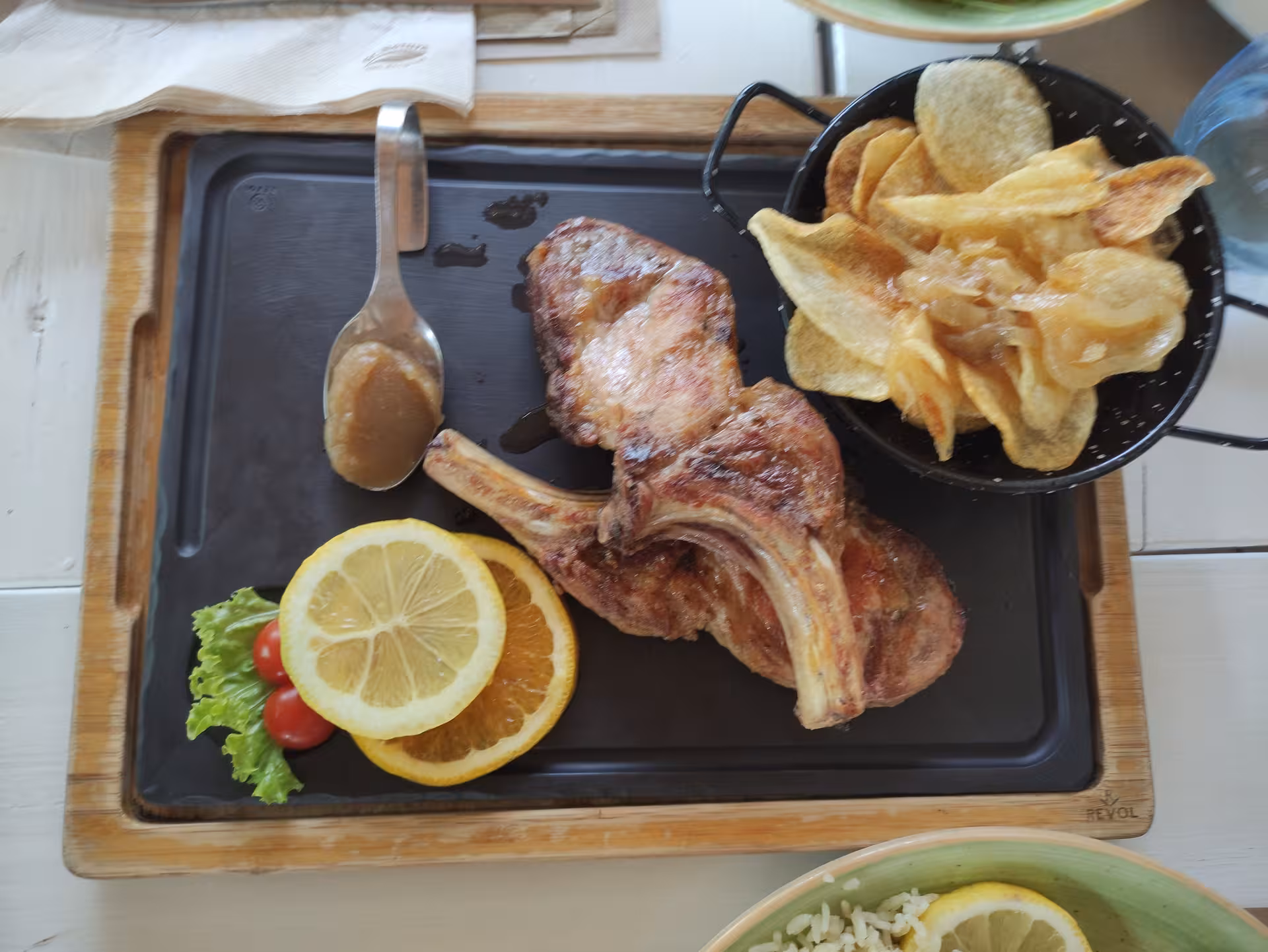 A delicious meal featuring grilled pork chops, citrus slices, and chips, perfect for savoring during a Monchique day trip.