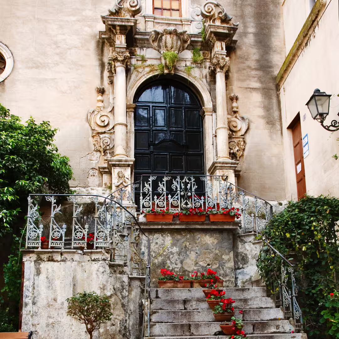 Baroque doorway and stone staircase with red geraniums in historic Monreale, Sicily, on a private tour from Palermo