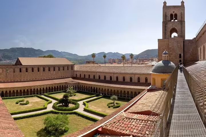 Panoramic view of Monreale Cathedral cloister gardens and bell tower with mountain backdrop on a private day trip from Palermo