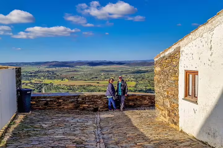 Visitors enjoying the scenic view of the Alentejo countryside from a cobblestone terrace in the historic village of Monsaraz.