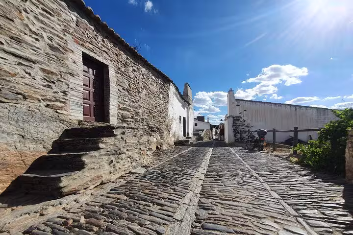 Charming cobblestone street in Monsaraz with rustic stone buildings under a clear blue sky, ideal for the Évora & Monsaraz tour.