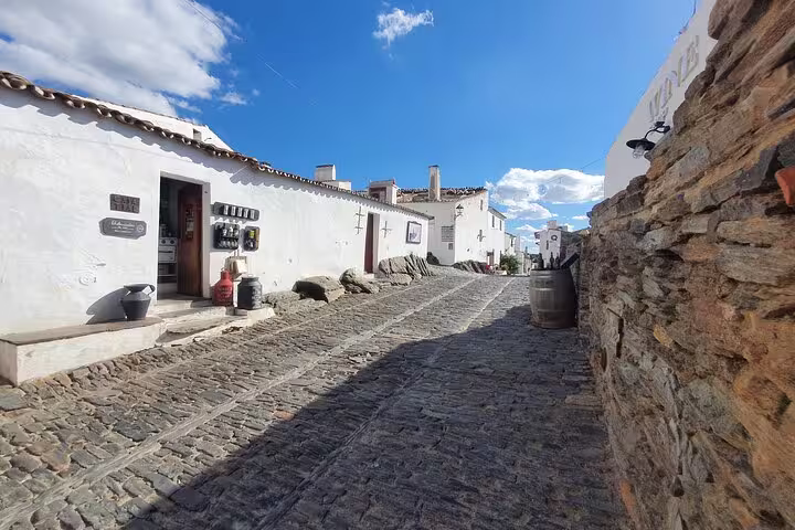 Charming cobblestone street in Monsaraz, Portugal, showcasing whitewashed buildings under a vibrant blue sky on a sunny day.