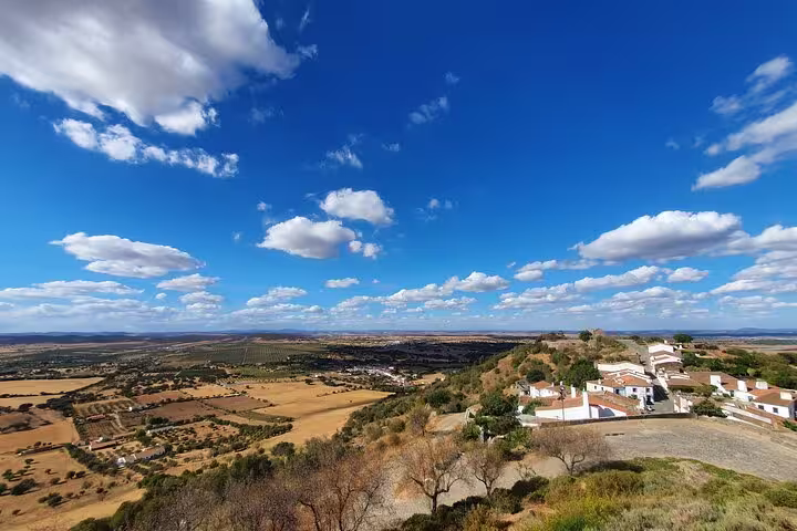Expansive view of Monsaraz village and surrounding Alentejo countryside under a vibrant blue sky on a sunny day.