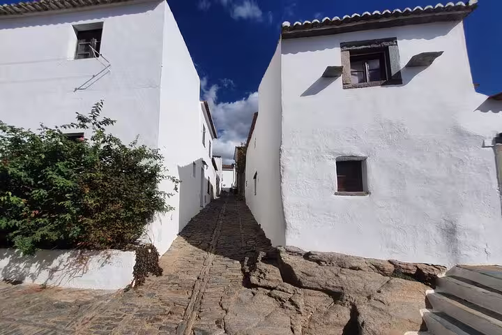 Charming narrow street with whitewashed houses in Monsaraz, Portugal, showcasing rustic architecture under a clear blue sky.