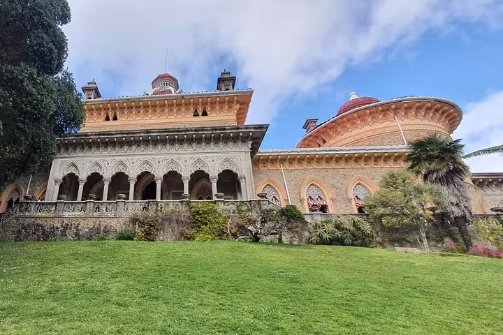 Stunning view of the Monserrate Palace in Sintra, featuring intricate architecture, lush gardens, and a clear blue sky.