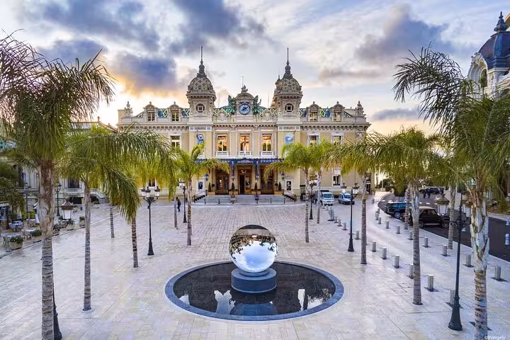 Majestic view of the iconic Monte Carlo Casino in Monaco, surrounded by palm trees at sunset on a French Riviera tour.