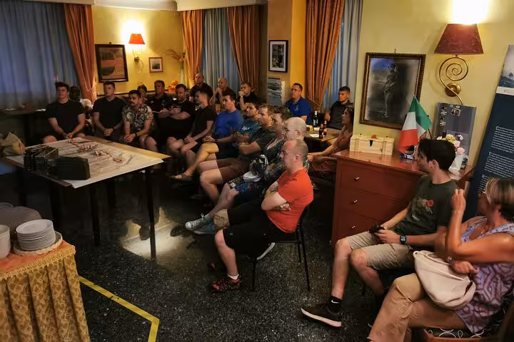 A group of people attentively listening to a historical presentation about Monte Cassino in a cozy room setting.