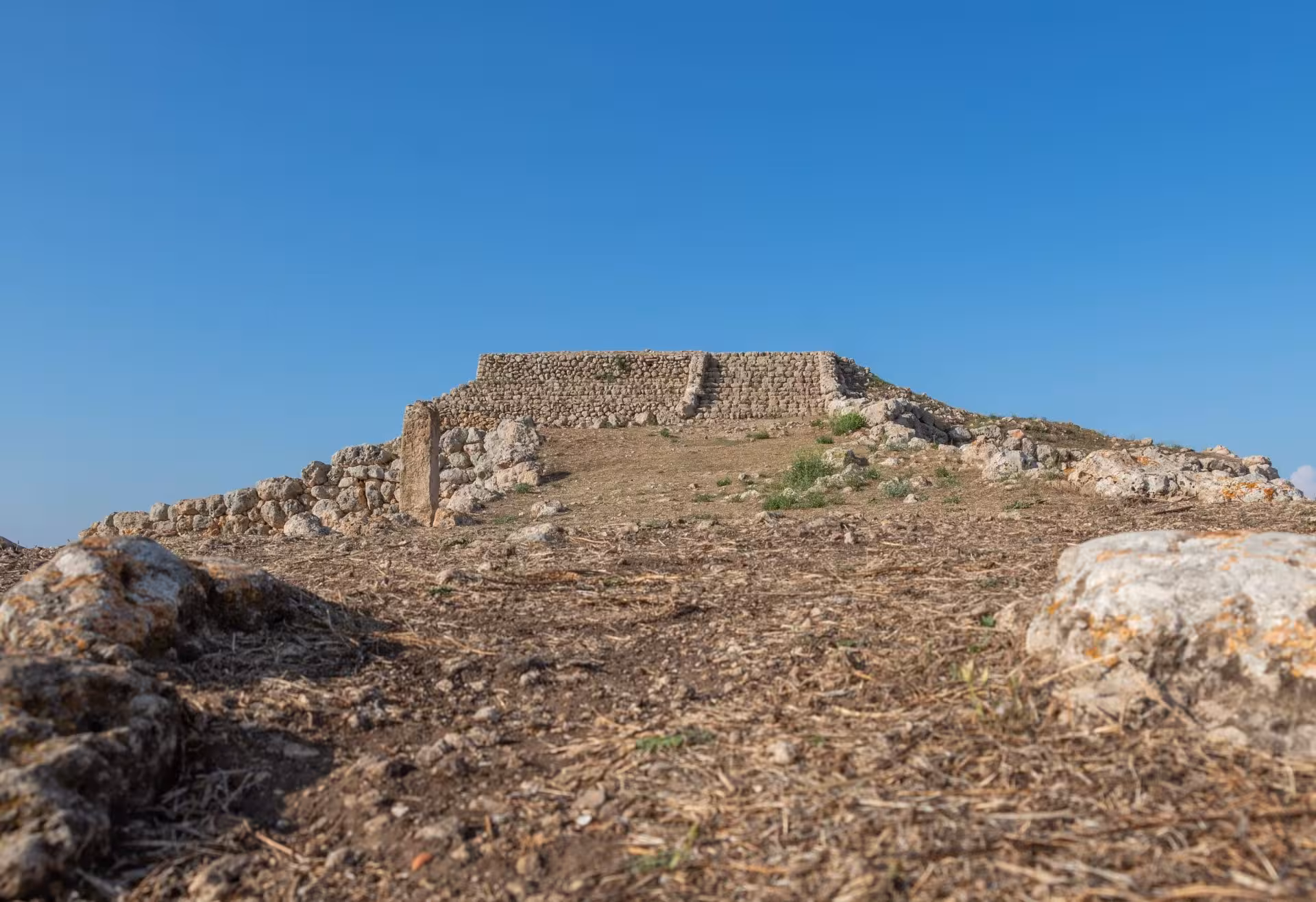 View of Monte d'Accoddi's ancient stone altar against a bright blue sky in Porto Torres.