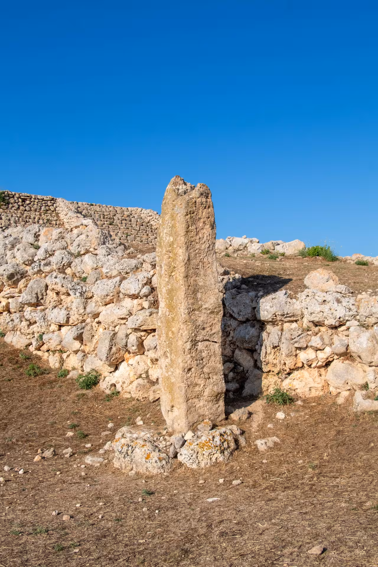 Ancient stone pillar at Monte d'Accoddi surrounded by rugged stone walls under a clear blue sky in Porto Torres.