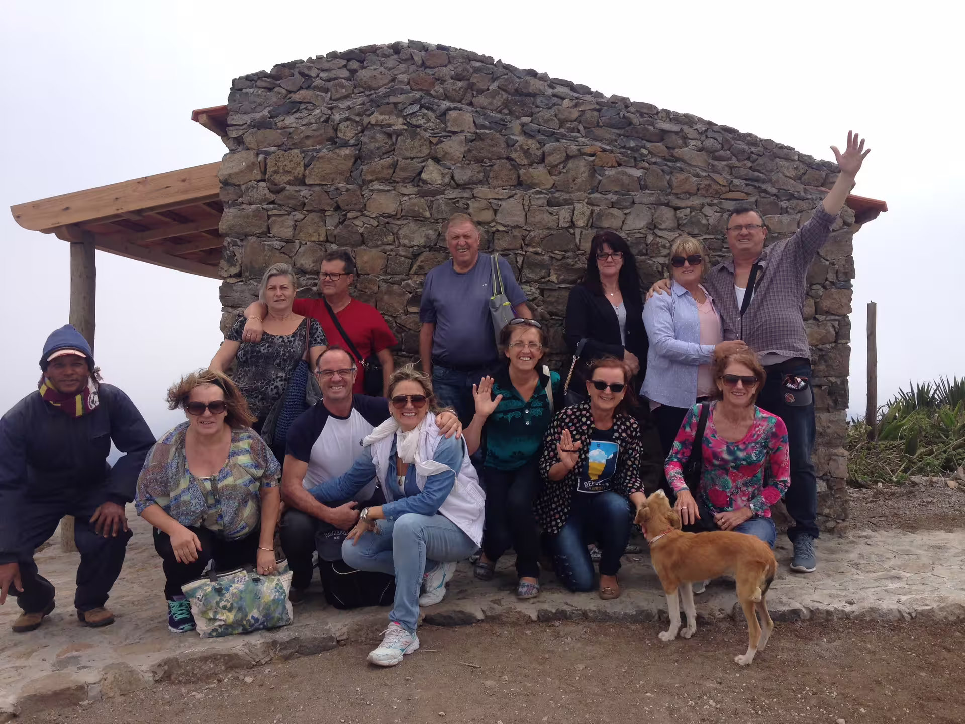 Group of tourists enjoying a scenic stop at Monte Verde, São Vicente, with rustic stone building and local guide in view.
