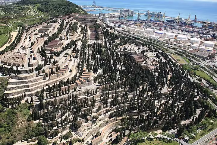 Aerial view of Montjuïc Cemetery with winding pathways, dense greenery, and Barcelona's port in the background.