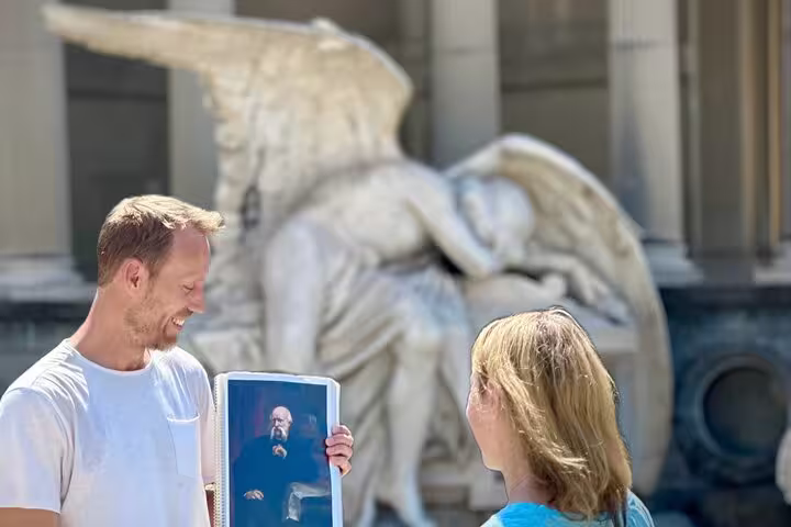 Tourists admire a historic angel sculpture and artwork at Montjuïc Cemetery, highlighting its artistic heritage.