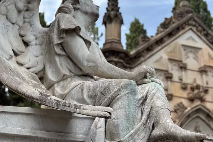 Exquisite angel statue seated beside ornate mausoleum at Montjuïc Cemetery, a highlight of the walking tour.