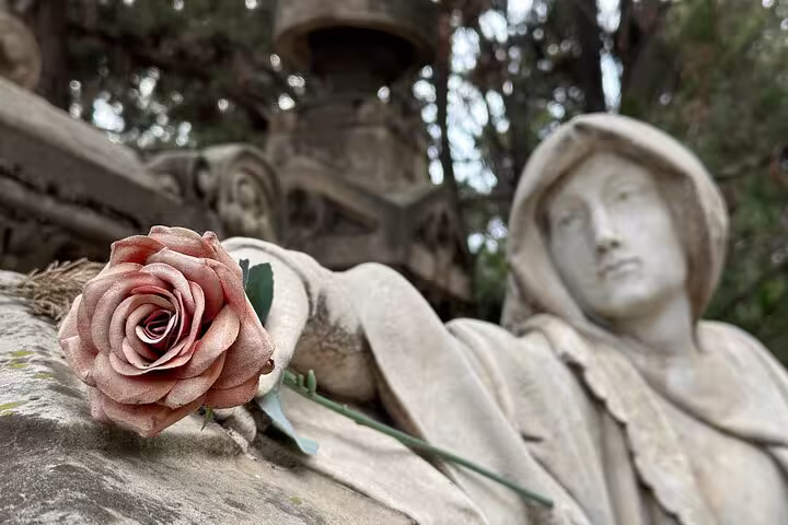 Close-up of a weathered statue with a rose, highlighting the intricate artistry found in Montjuïc Cemetery.