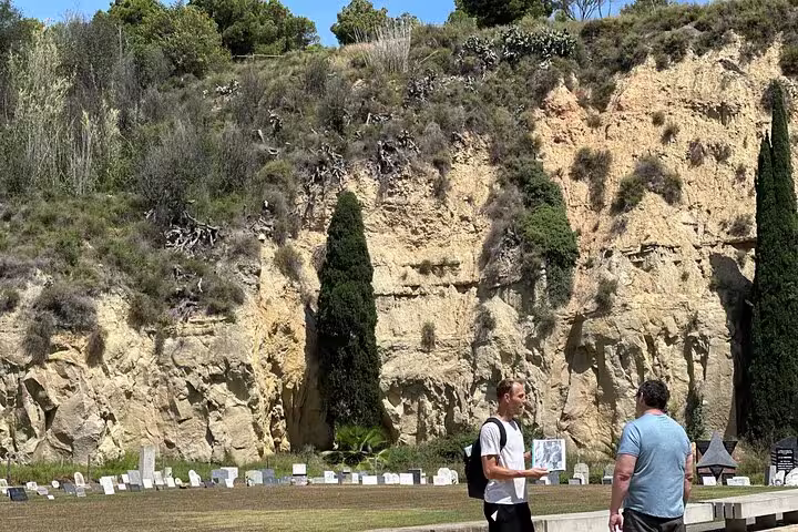 Tour guide showing map to visitor against rocky backdrop at Montjuïc Cemetery Walking Tour, highlighting history and nature.
