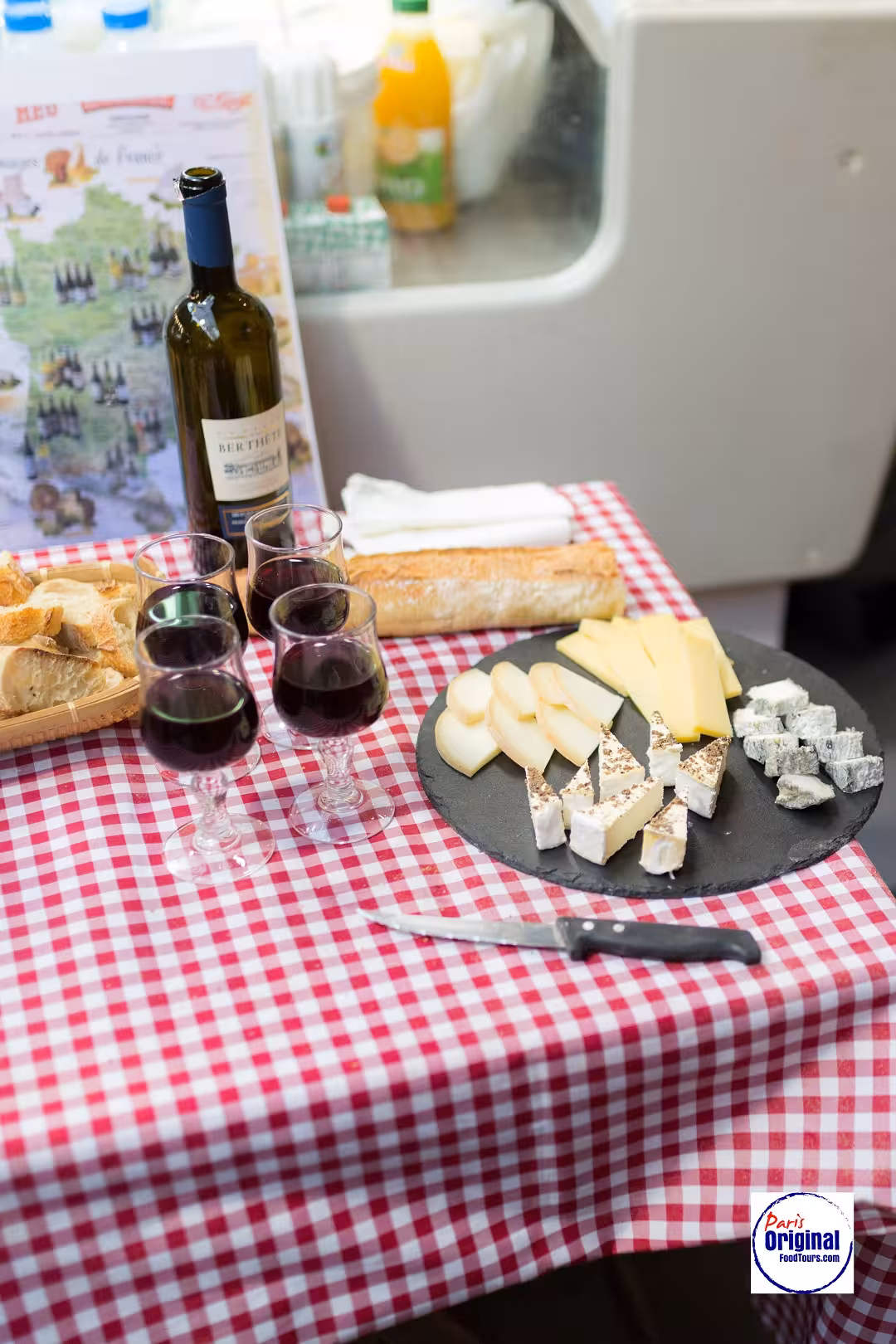 A spread of French wine, cheese, and bread on a checkered tablecloth, perfect for Montmartre wine tasting tours.